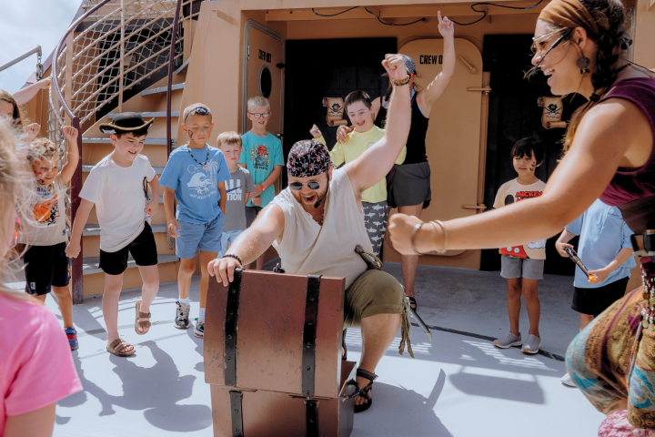 Pirate-themed performance with kids cheering around a treasure chest on a ship deck.