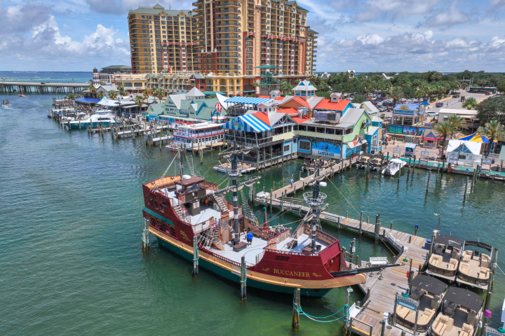 Aerial view of a marina with a pirate ship and colorful buildings nearby.