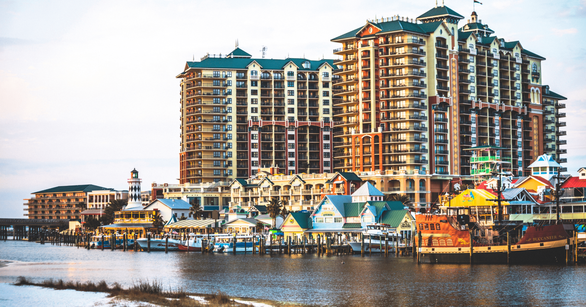 Colorful waterfront buildings and pirate ship in front of tall condos by a harbor.