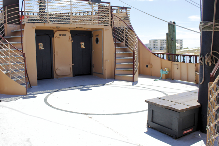 Ship deck with stairs leading to a raised platform and two 'crew only' doors, a wooden chest, and ocean view.
