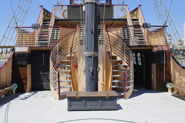 Deck of a vintage ship with twin spiral staircases and rigging.