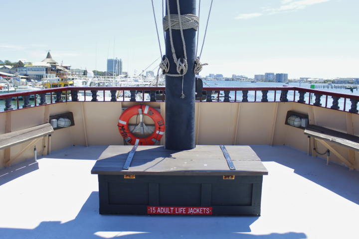 Boat deck with wooden benches, life preserver, and storage box; cityscape and marina in background.