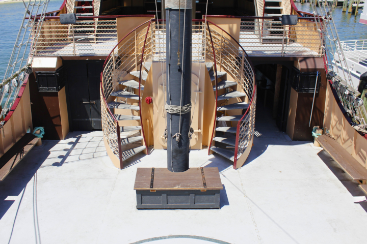 Ship deck with spiral stairs, central mast, and wooden storage chest.