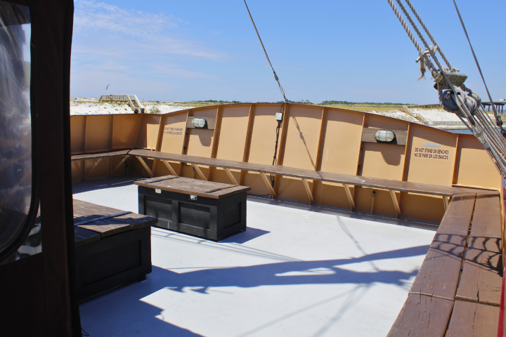 Empty ship deck with benches and a wooden chest under a clear blue sky.