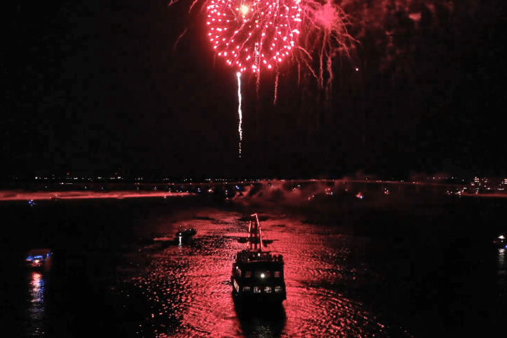 Boat on water with large red fireworks display in night sky.