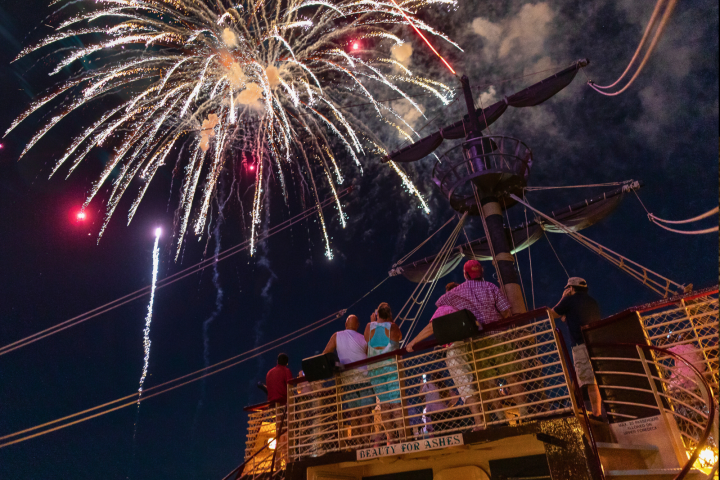 People on a ship deck watching fireworks explode in the night sky.
