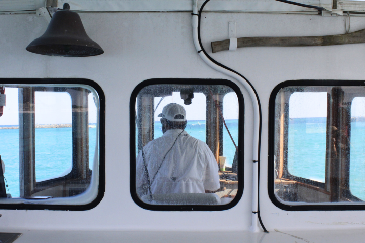 Boat captain seen from behind through large windows, overlooking the ocean.