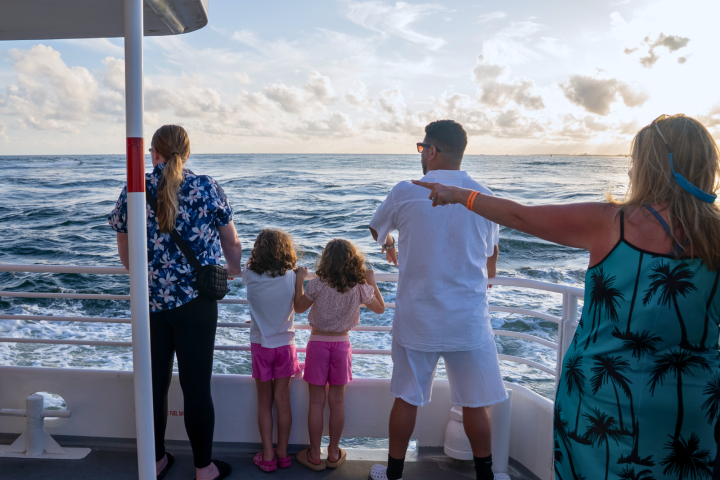 People looking at the ocean from a boat's deck during sunset.