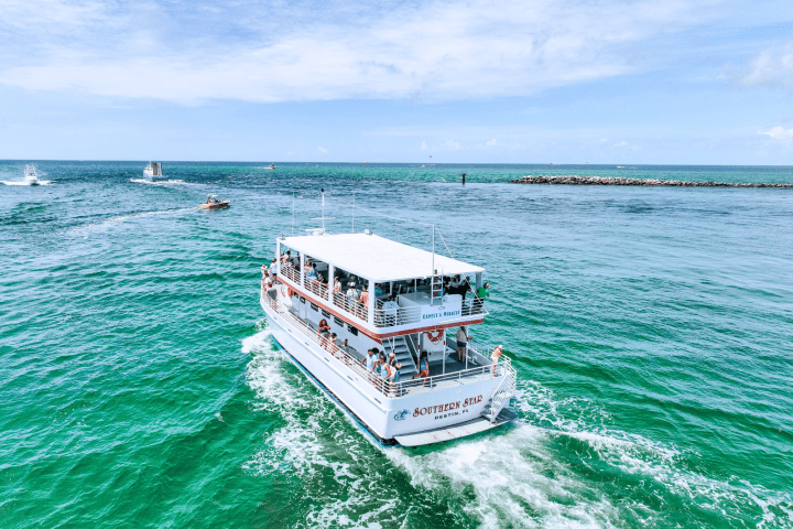 Tour boat on clear ocean water under a blue sky with passengers on deck.