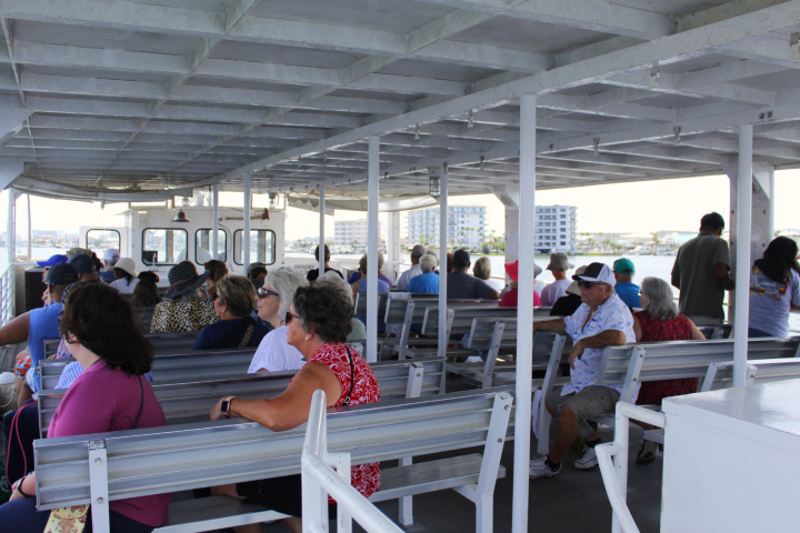People seated on a boat with benches, wearing casual summer clothing.