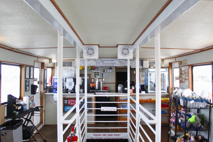 Interior of a ferry with a snack bar, handrails, and large windows on both sides.