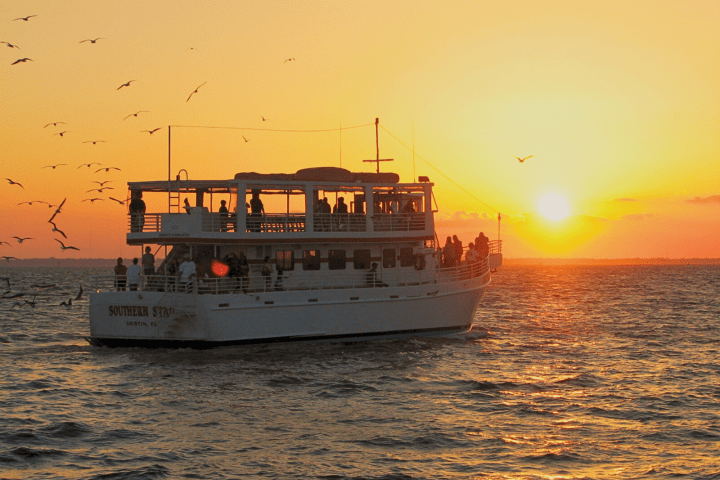 Boat at sunset with seagulls flying over the ocean.