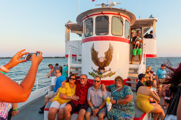 Group of people posing on a boat deck with American flag and eagle emblem at sunset.