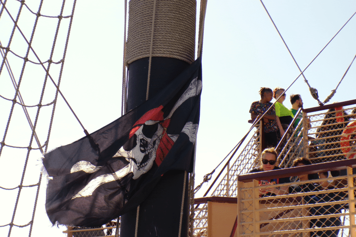Pirate flag on ship mast with people on deck.