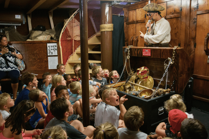 Pirate entertainer with treasure chest performing for children in a ship's cabin.