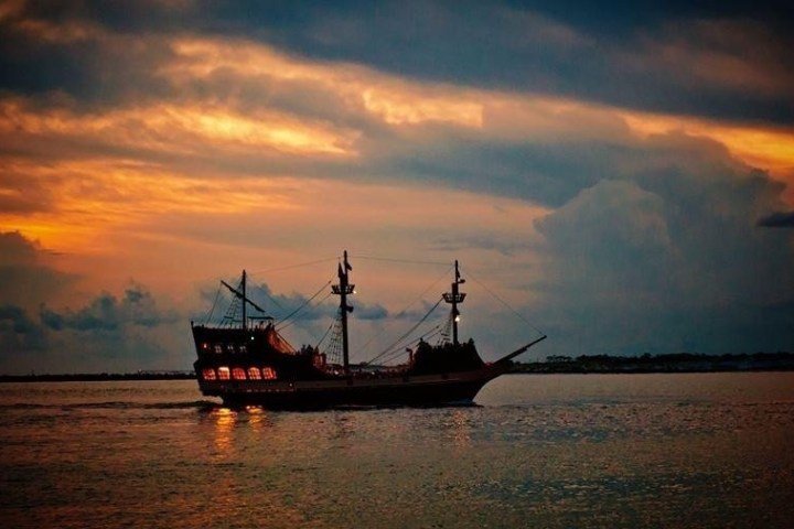 Silhouette of a tall ship on the ocean at sunset, with orange and blue clouds.
