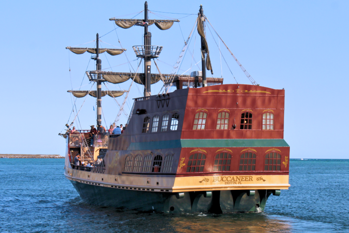 A pirate-style ship named Buccaneer sailing in clear blue water with people on deck.