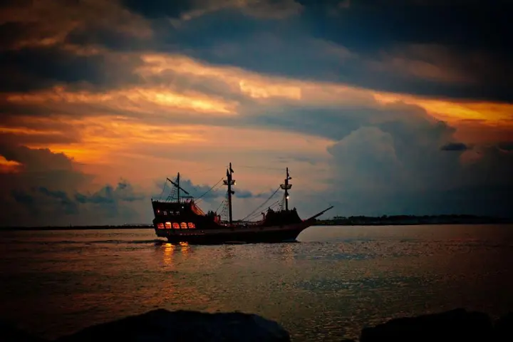 a large pirate ship sailing the ocean at sunset