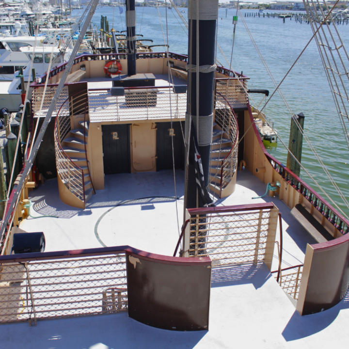 Top deck of a moored ship with spiral stairs and railing, overlooking water and boats.