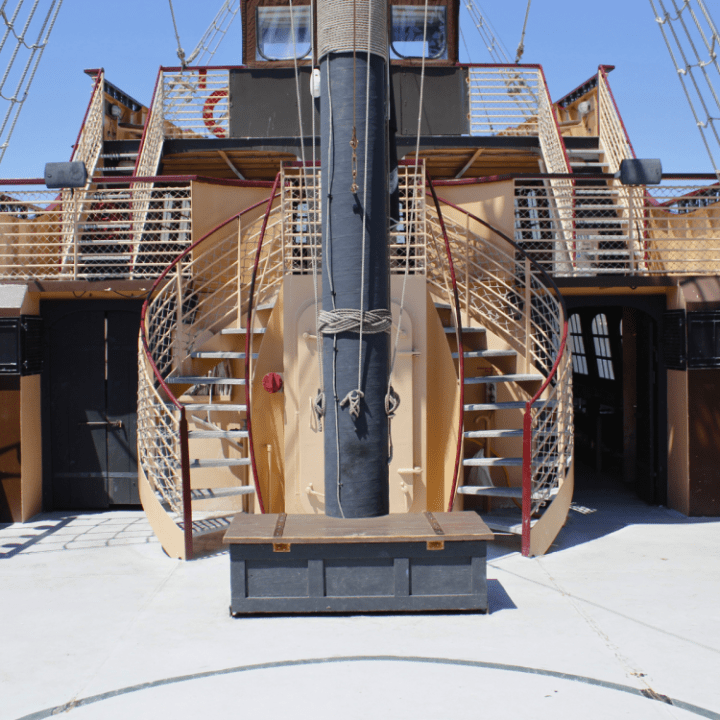 View of ship deck with two curved staircases and mast in center.