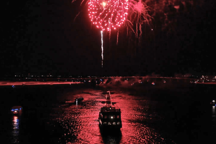 Boat on water with red fireworks in the night sky.
