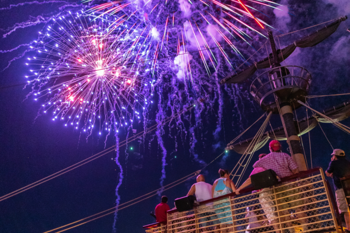 People on a ship deck watching colorful fireworks in the night sky.
