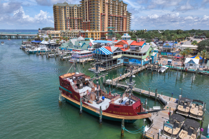 Colorful buildings and pirate ship at a coastal marina with tall hotel in background.