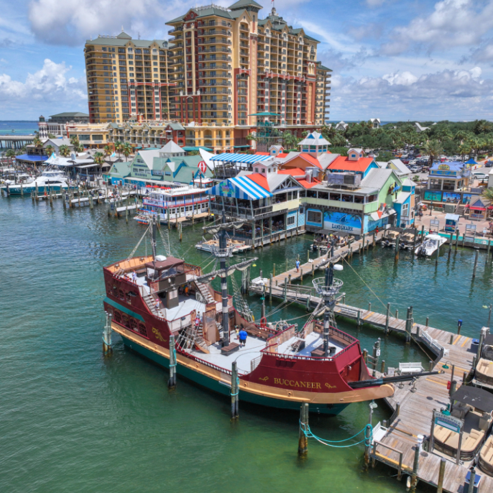 Colorful buildings and pirate ship at a coastal marina with tall hotel in background.