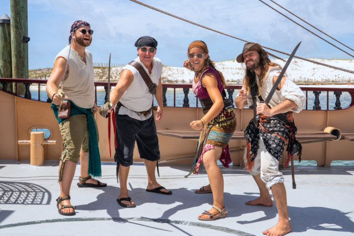 Four people dressed as pirates posing with swords on a ship deck.