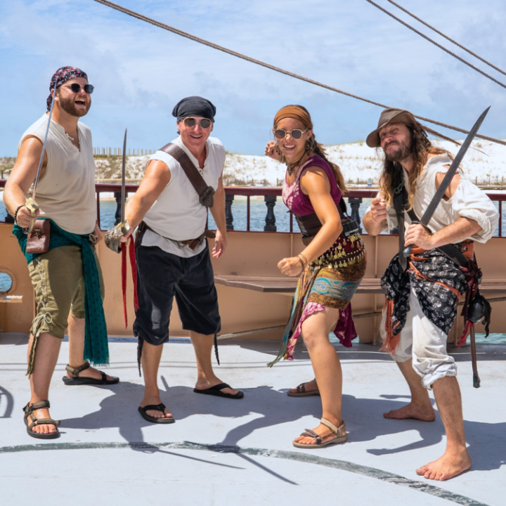 Four people dressed as pirates posing with swords on a ship deck.