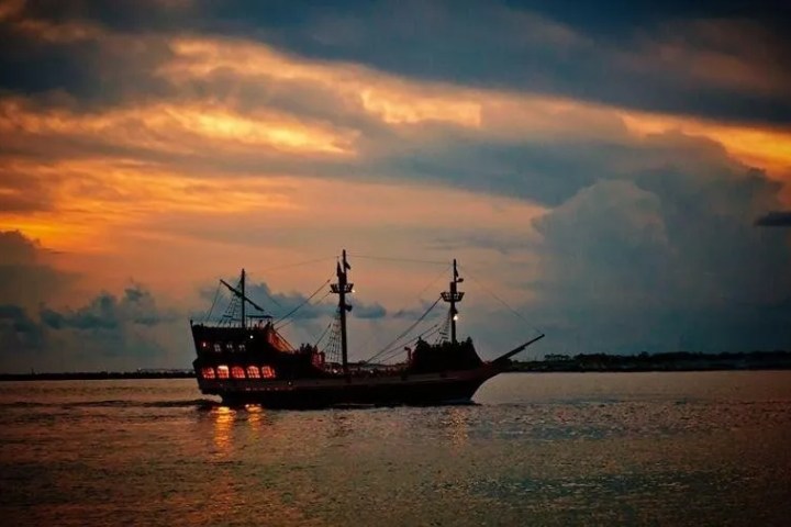 Silhouette of a pirate ship at sunset on the ocean.