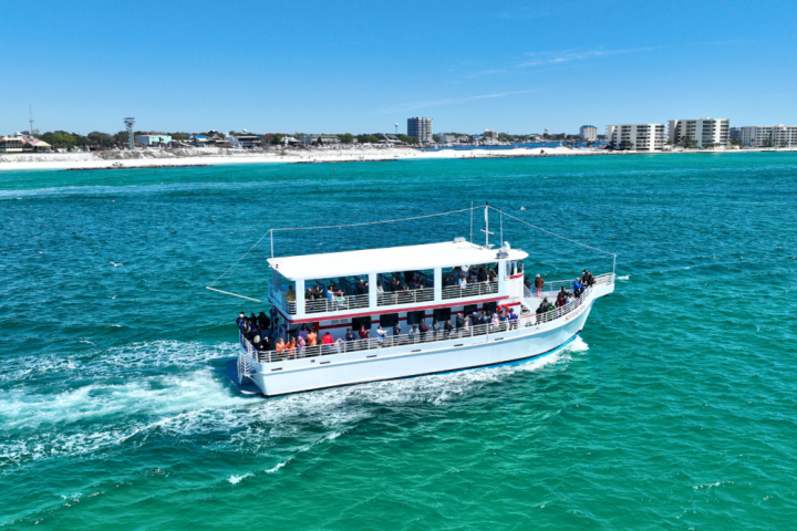 A white tour boat filled with people cruising on turquoise water near a city shoreline.