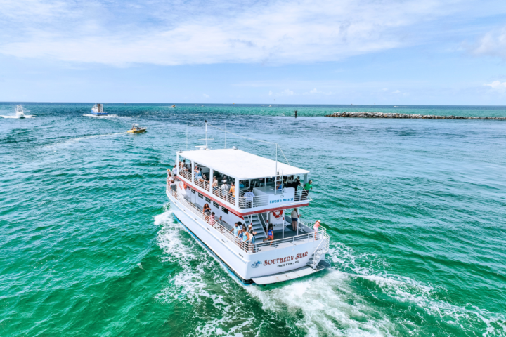 A tour boat sails on clear turquoise water under a partly cloudy sky.