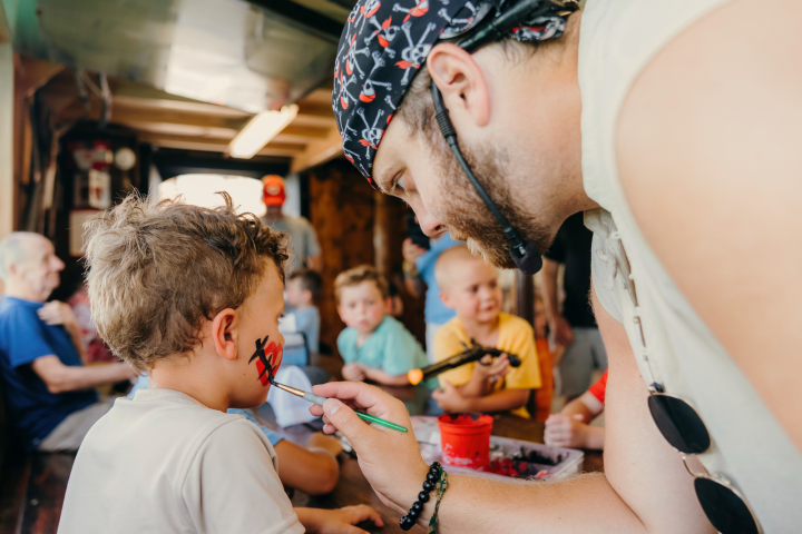 Man painting a child's face in a busy craft area with others around.