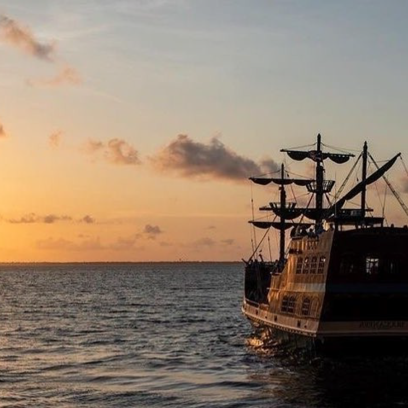 a pirat eship cruising towards a sunset over a body of water