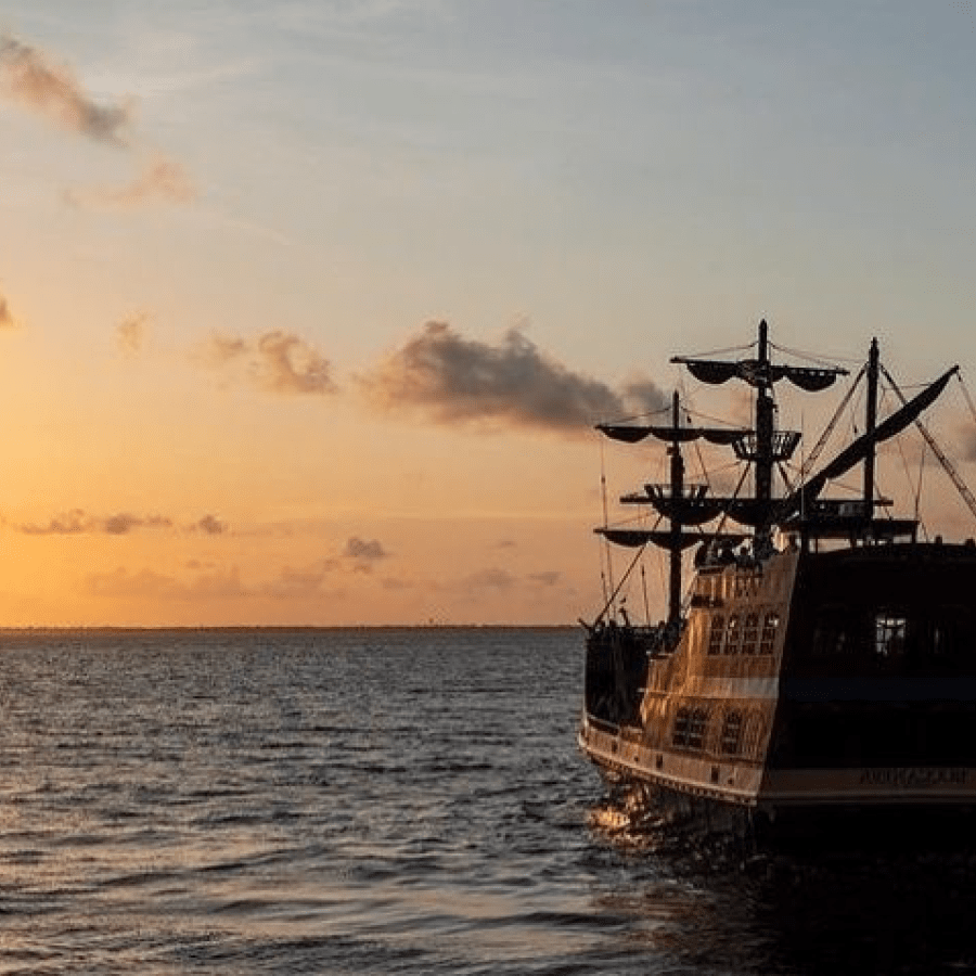 a pirat eship cruising towards a sunset over a body of water